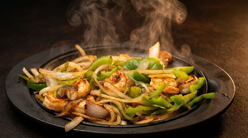 Sizzling shrimp fajitas with green peppers and onions on a hot cast iron plate, emitting steam.