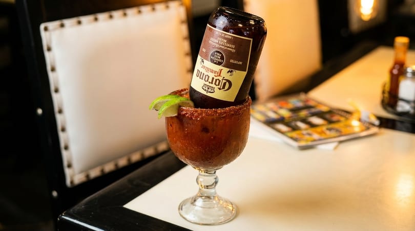 Corona Familiar beer bottle upside down in a michelada glass with lime wedges.